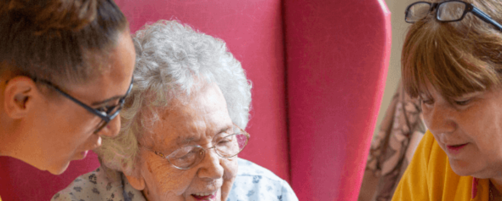 An elderly lady reading with staff in a care home - Applewood Healthcare