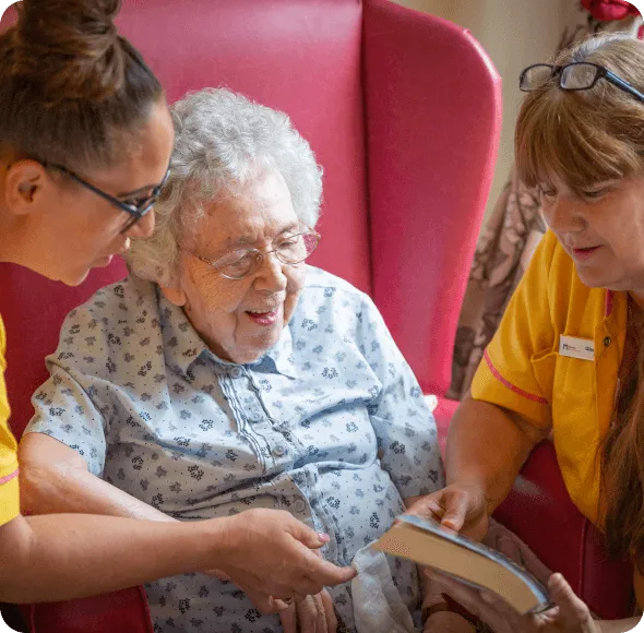 An elderly lady reading with staff in a care home - Applewood Healthcare