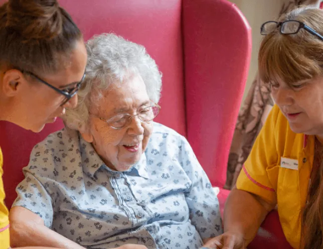 An elderly lady reading with staff in a care home - Applewood Healthcare