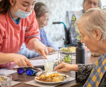 A nurse assisting a disabled resident with cutting up food - Applewood Healthcare