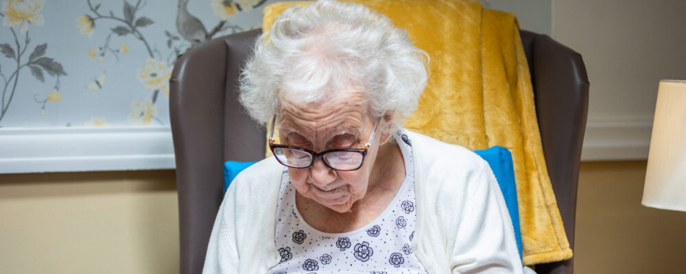 An elderly resident knitting in a comfy chair at care home - Applewood Healthcare